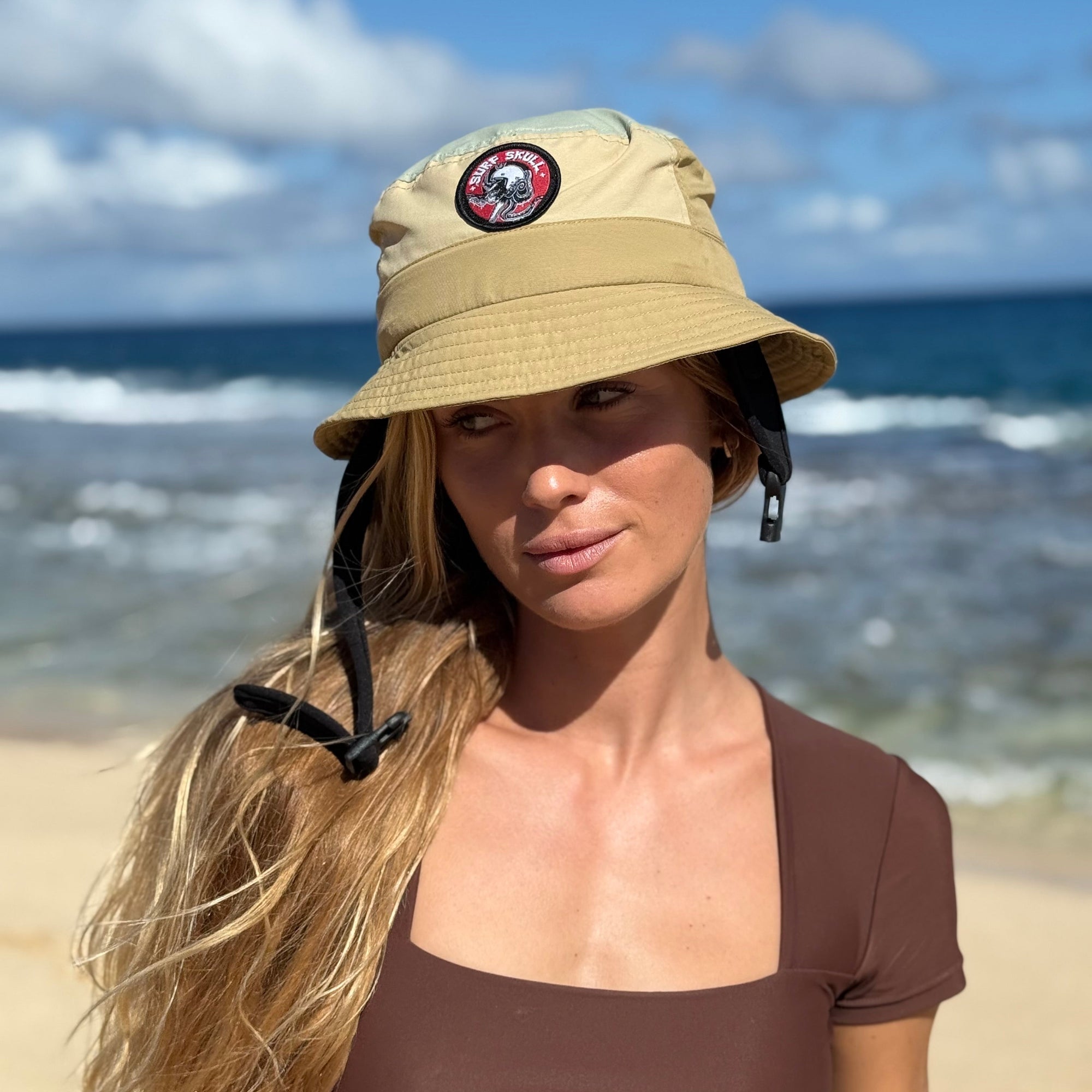 Woman wearing a beige bucket hat with a logo on a beach


